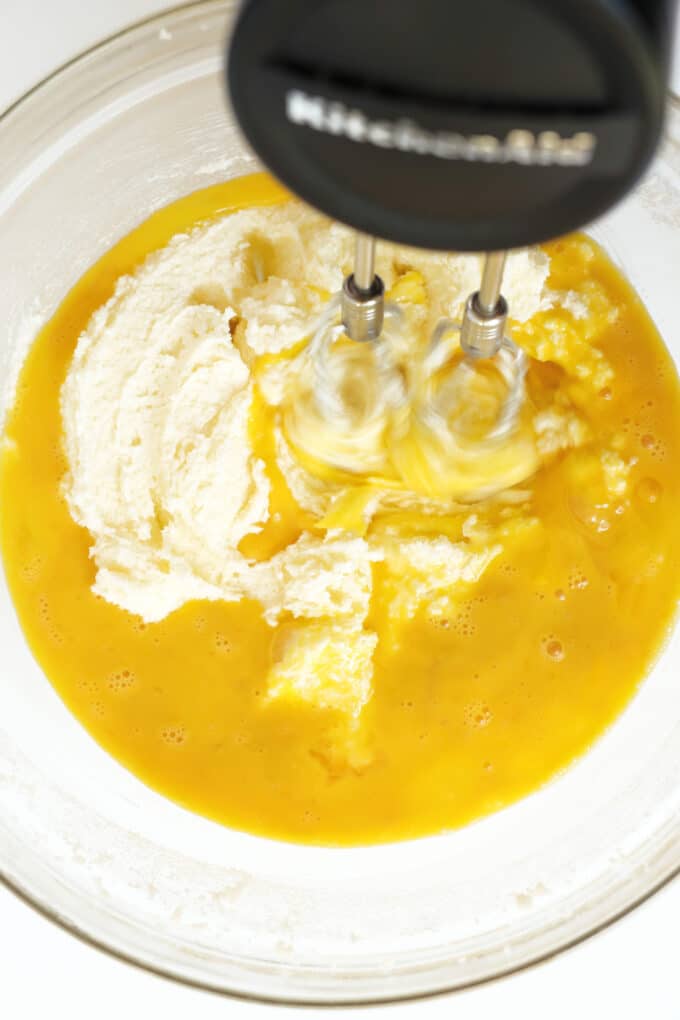 The egg and vanilla mixture being mixed into the creamed butter and sugar with a hand mixer.