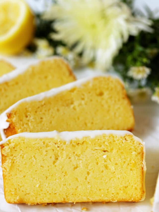 A few vibrant yellow slices of Lemon Pound Cake laying against each other, with a bouquet of flowers laying on the counter behind them.