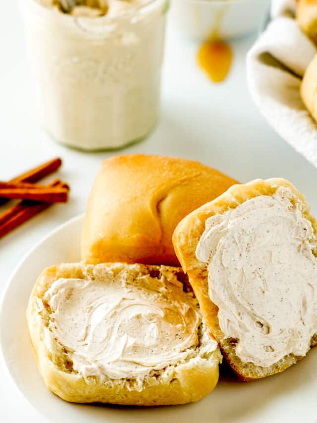 One whole roll with another one that is sliced lying next to it on a white plate. In the background is a jar of Texas Roadhouse butter.