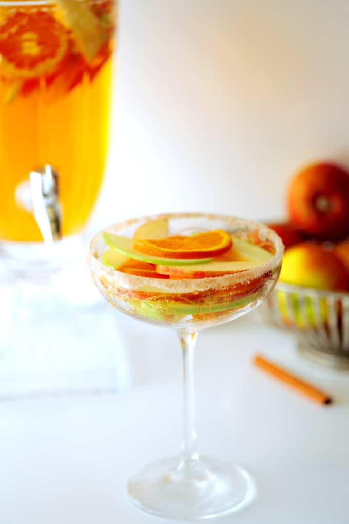 A wine glass with a cinnamon sugar rim and sliced apples and oranges inside. 