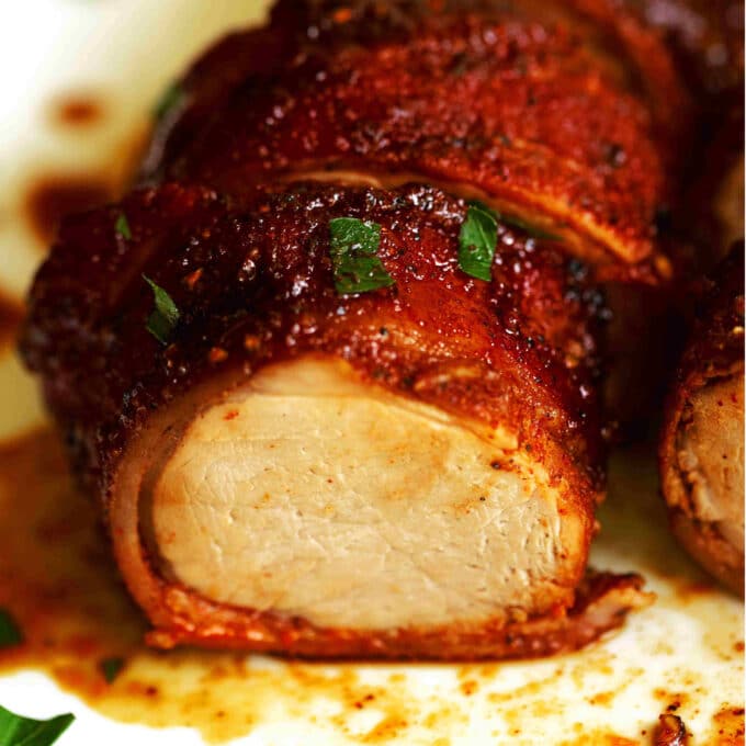 A close up of a slice of Bacon Wrapped Pork Tenderloin on a white surface. 