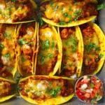 An overhead look at a pan full of Baked Tacos with melty cheese and chopped cilantro on top. There is a small dish of pico de Gallo beside them.