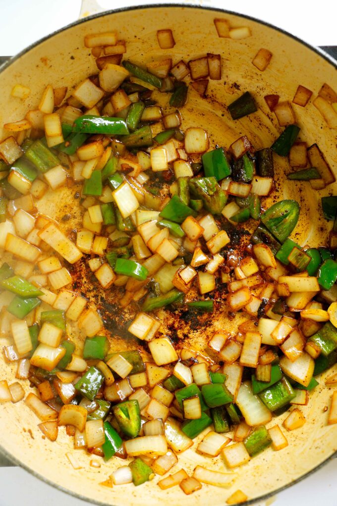 An overhead look at diced onion and jalapeño being sautéed in a pan with oil.