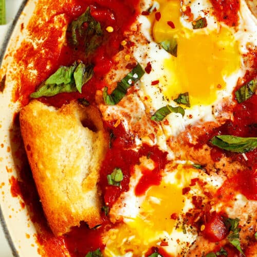 A close up of a pan of Eggs In Purgatory with a piece of baguette stuck into the sauce.