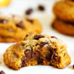A close up of a Pumpkin Chocolate Chip Cookie with a bite taken out of it. It is soft and full of melty chocolate chips.