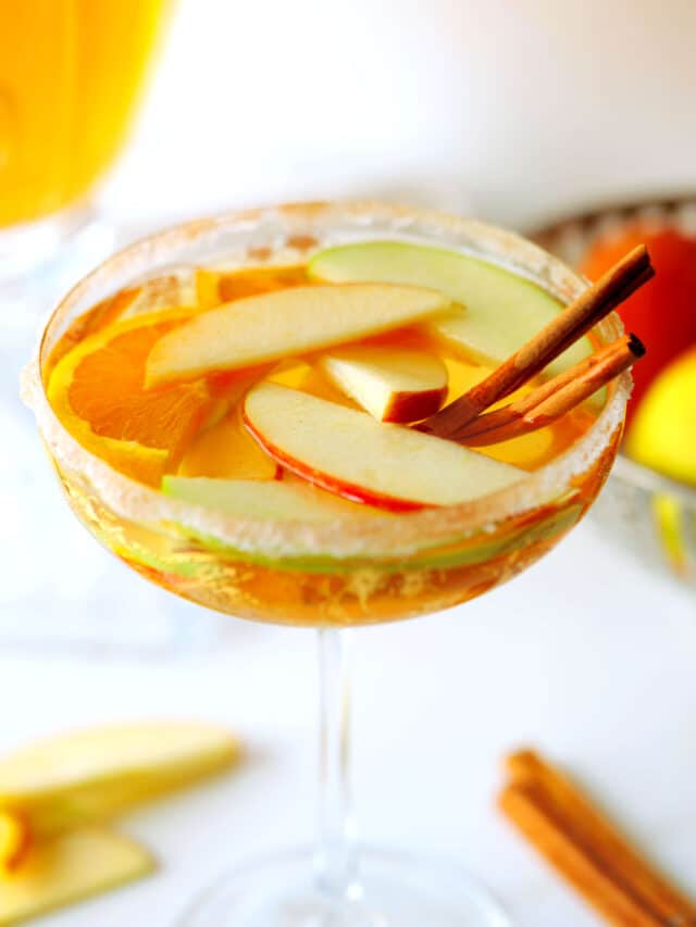 A wine glass full of Apple Cider Sangria with apple and orange slices floating in it and cinnamon sticks on the side.