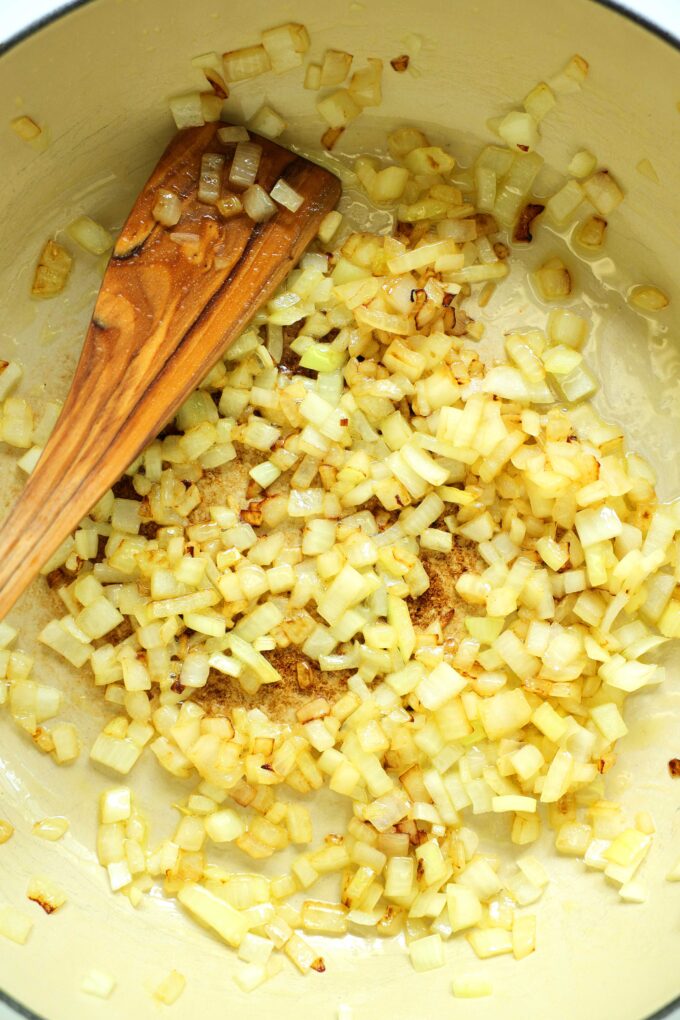 Diced onion being sautéed in a pan with oil and a wooden spatula.