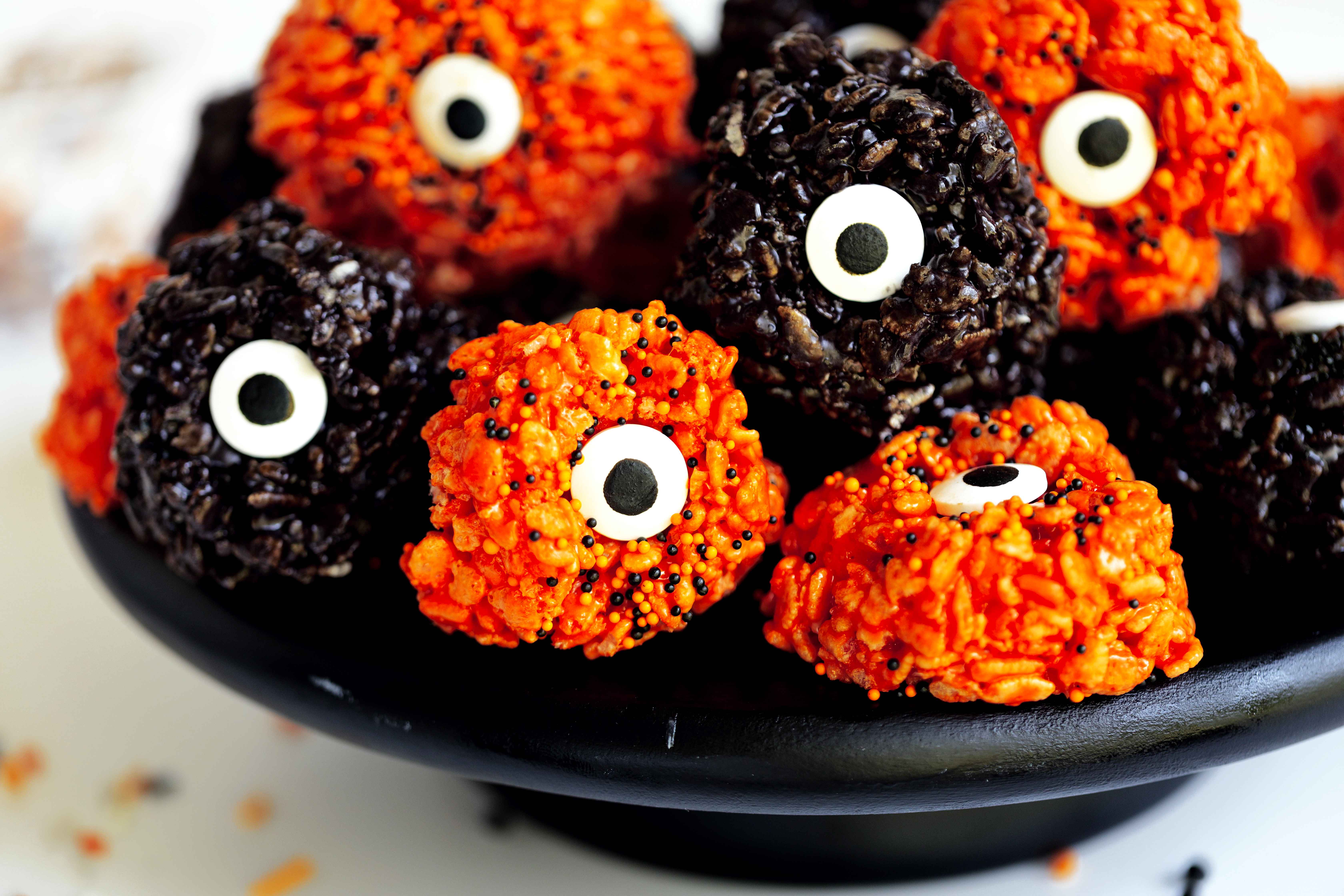 Black bowl on a white surface holding a stack of black and orange rice krispie eyeballs topped with round black sprinkles.