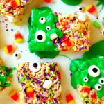 Five rice krispie treats cut in to rectangles atop a white surface. Rice krispies are topped with green, purple, and white sprinkles, candy corn, marshmallows, black-and-white eyeballs