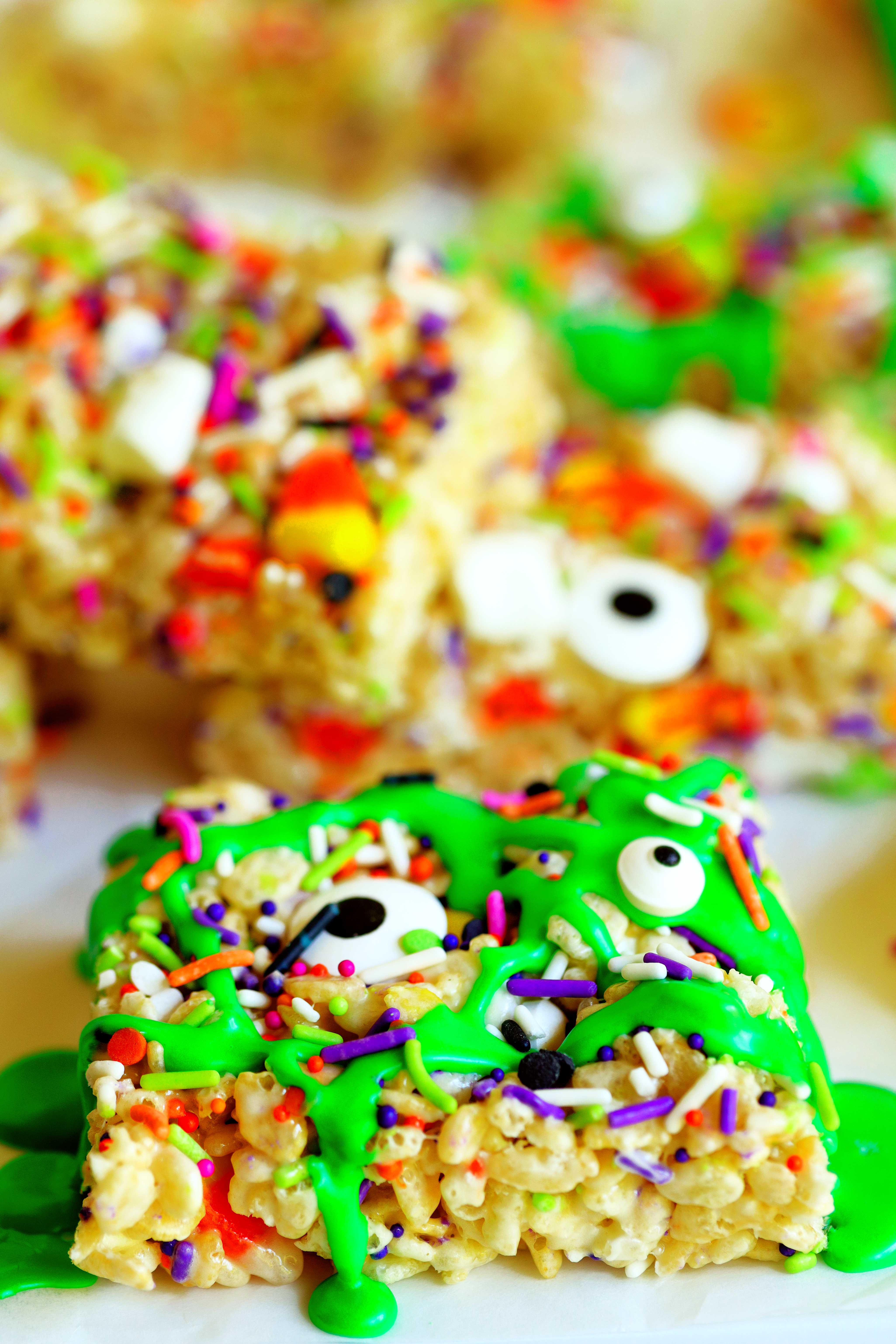 Rice krispie treat covered in green icing to look like slime, topped with multi-colored sprinkles. Two black-and-white eyeballs--different sizes--size on top of the green icing.