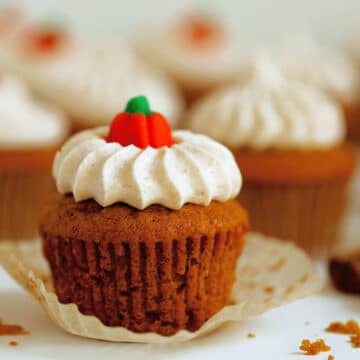 A single Pumpkin Muffin sits in the foreground with the cupcake liner peeled down and a pumpkin candy on top. There are other cupcakes sitting in the background.