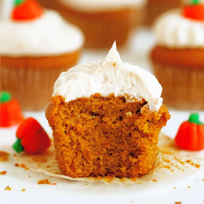 A close up of a Pumpkin Cupcake with a bite taken out of it and pumpkin candies scattered around it.