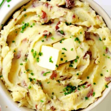 Overhead view of mashed potatoes topped with two squares of butter and chives in a mixing bowl.
