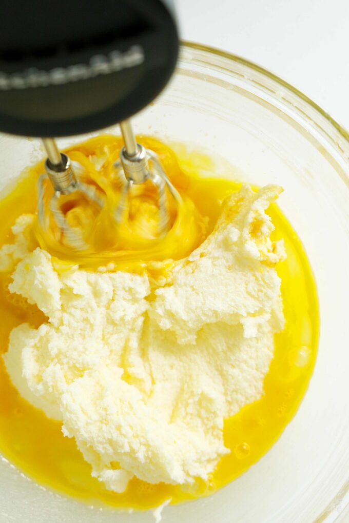 A hand mixer being used to mix eggs into the creamed butter and sugar mixture.