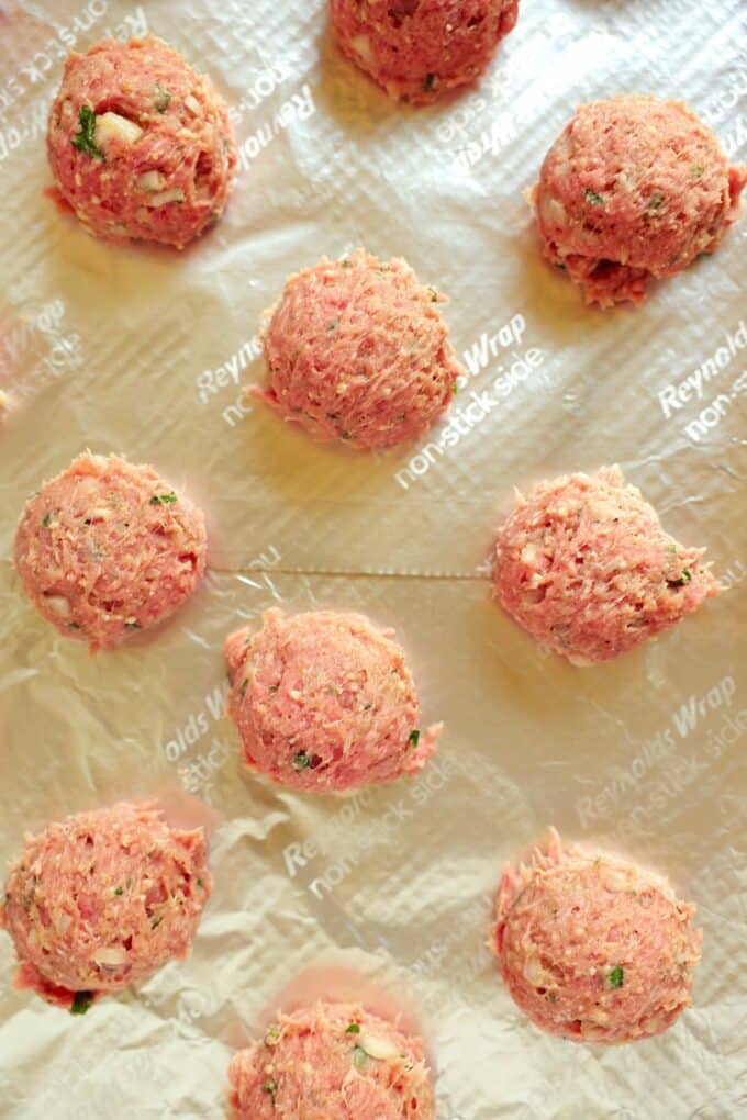 An overhead view of uniform balls of the turkey mixture lined up on a foil-lined baking sheet.