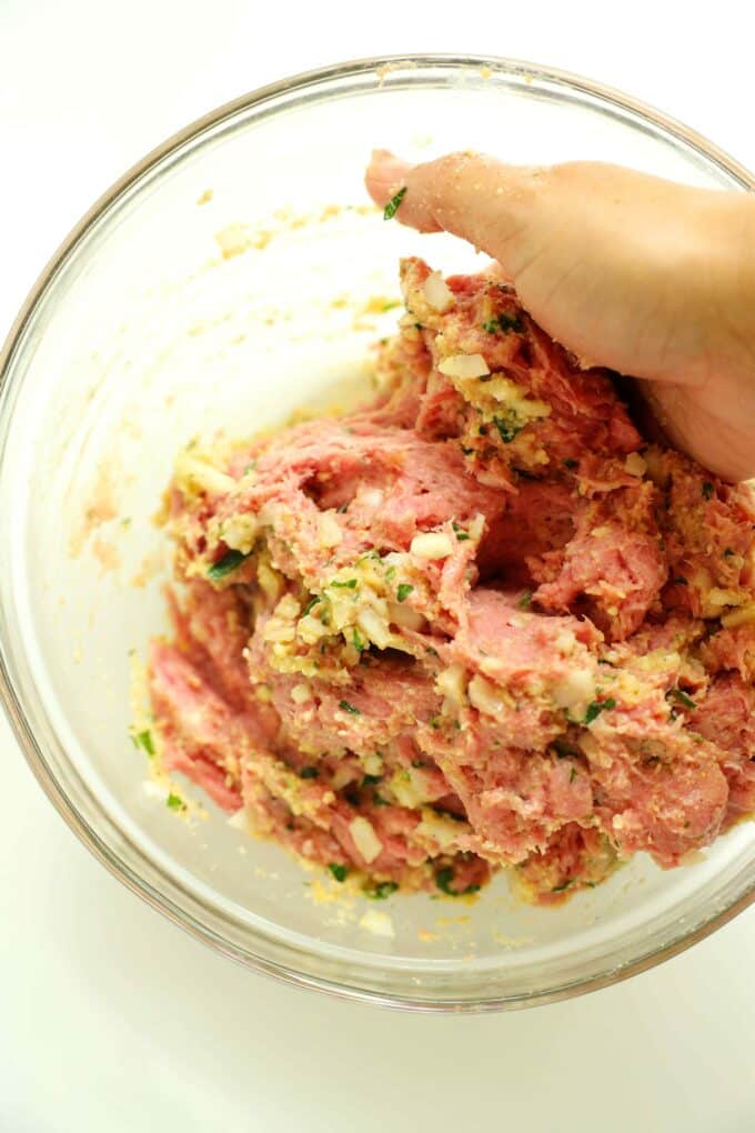 A hand mixing ground turkey into the milk and breadcrumb mixture.