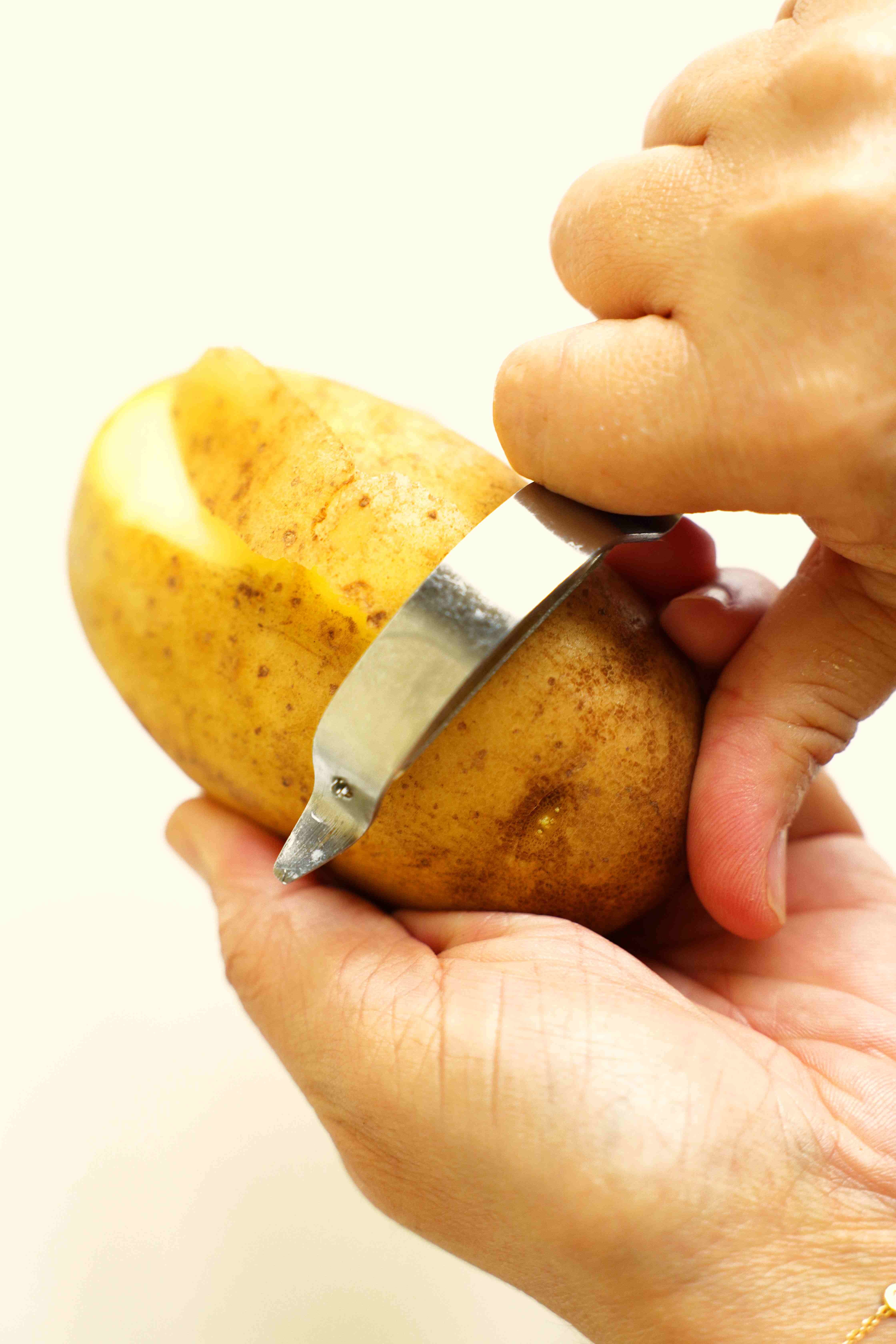 Hands holding a russet potato, with potato peeler peeling it.