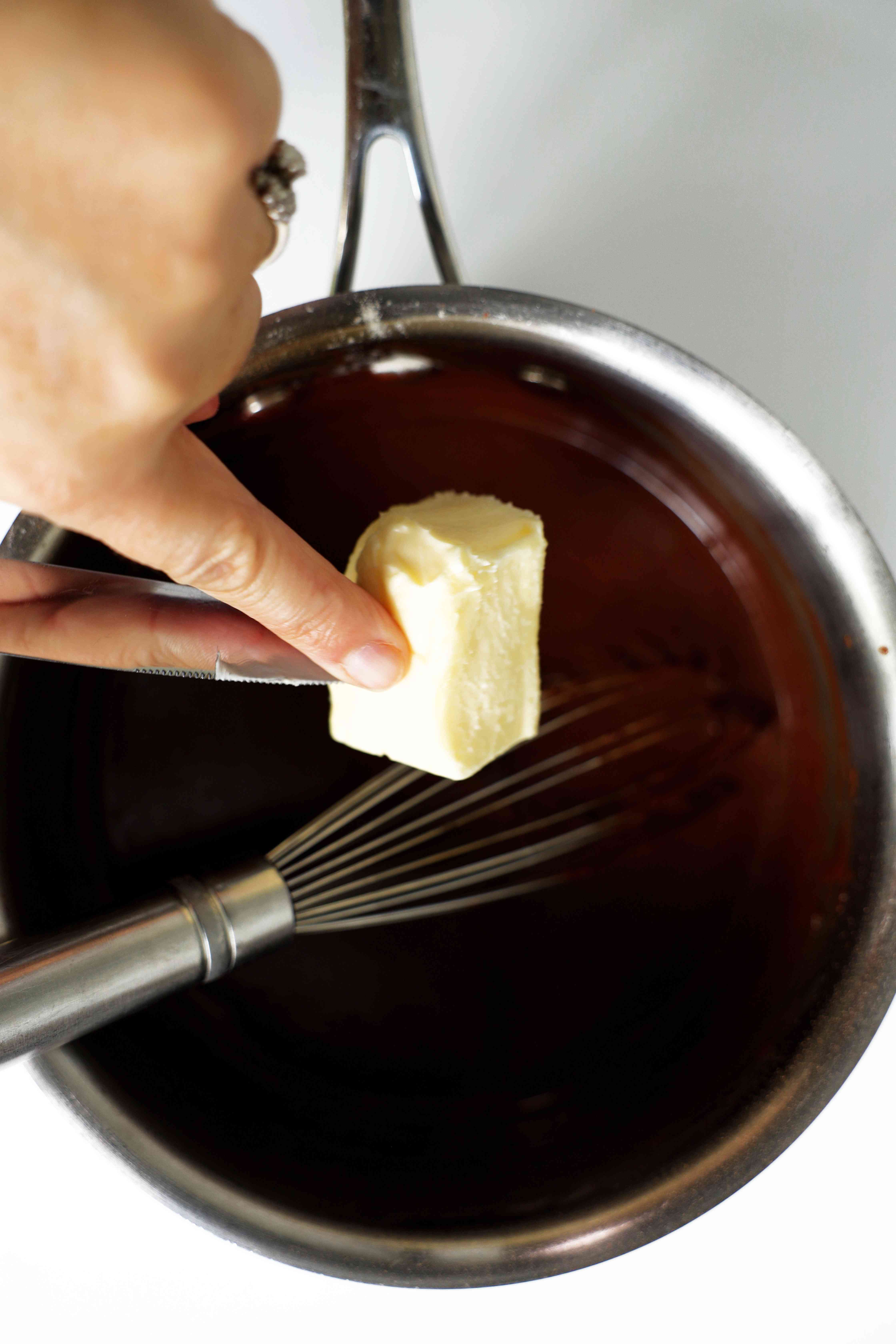 Butter being poured into the Chocolate Gravy mixture, in a saute pan with a whisk.