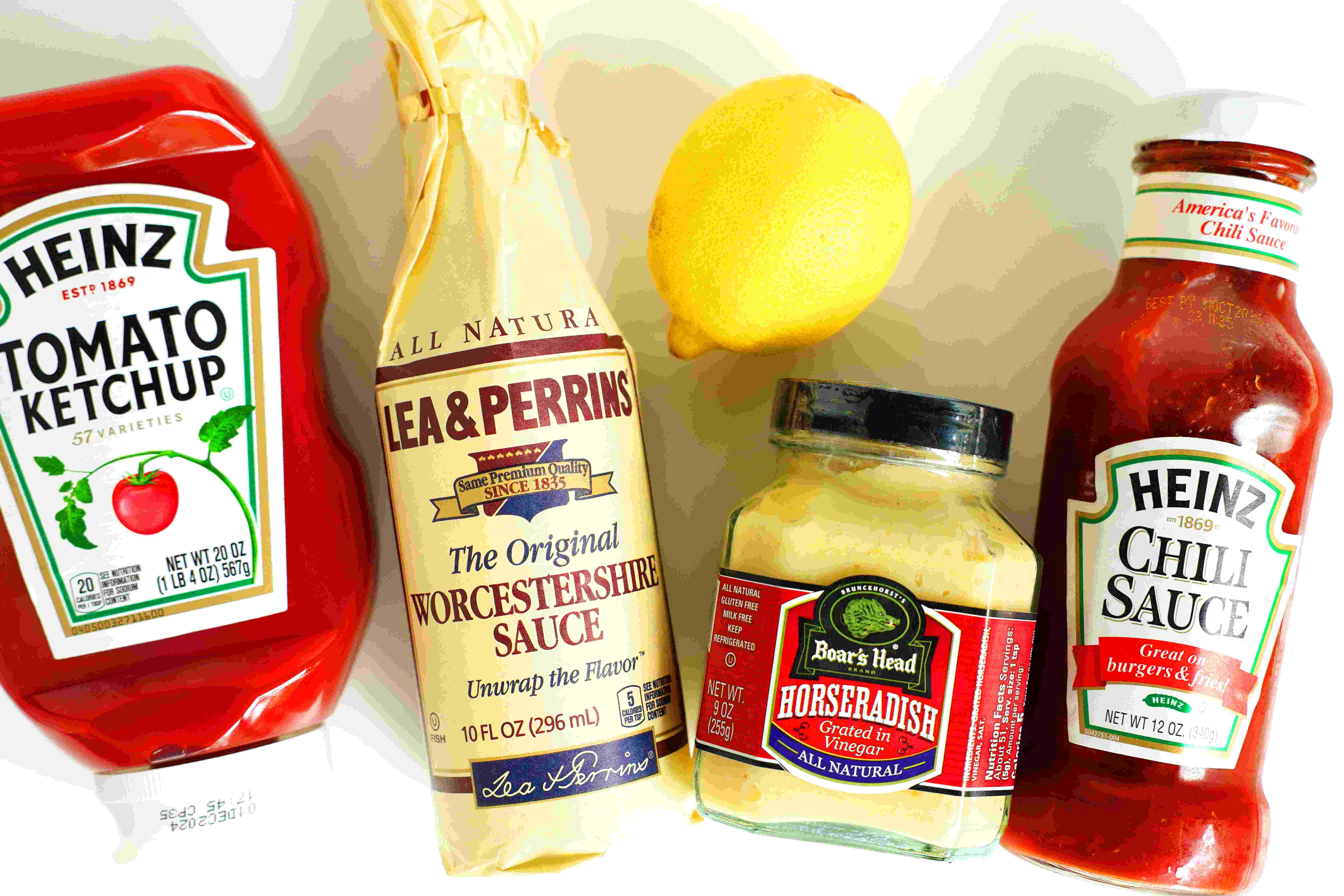 Ingredients for Shrimp Cocktail Recipe lined up together on the countertop: ketchup, Worcestershire sauce, horseradish, chili sauce, and lemon