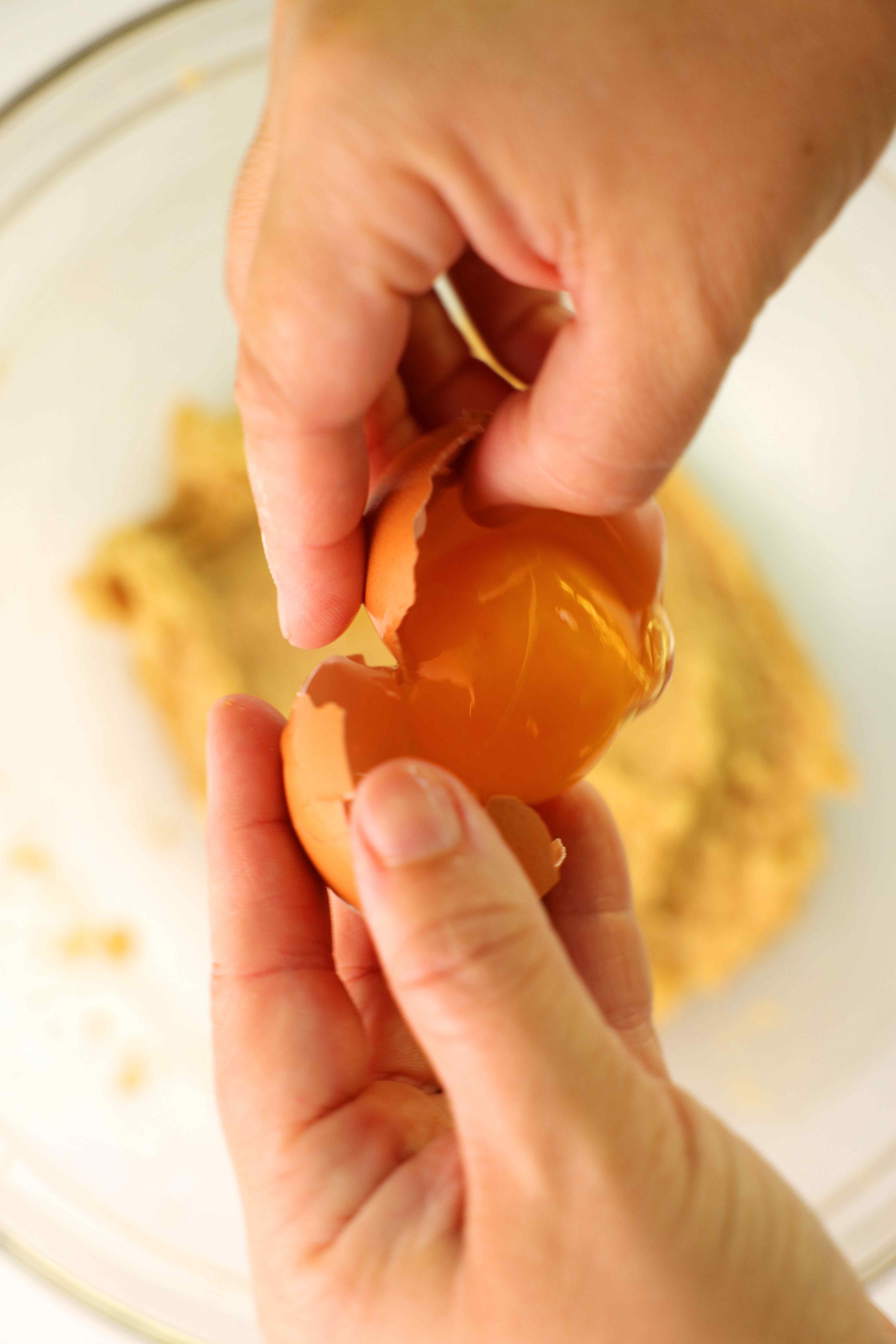 Two hands are cracking an egg into the cookie ingredients.