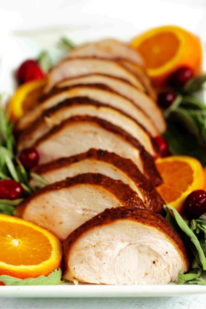 Sliced Smoked Turkey Breast on a platter with rosemary, cranberries, and orange slices