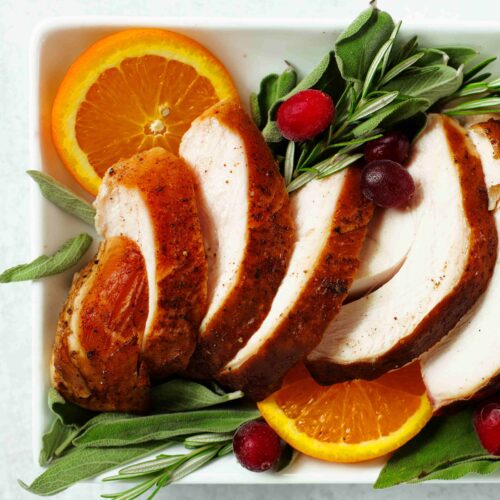 Sliced Smoked Turkey Breast on a platter with rosemary, cranberries, and orange slices