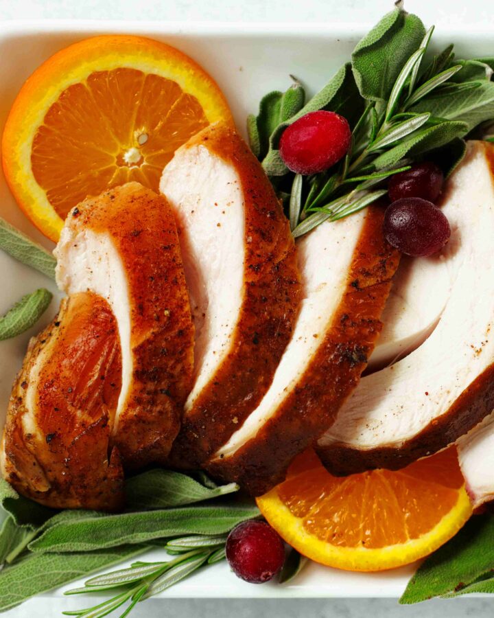 Sliced Smoked Turkey Breast on a platter with rosemary, cranberries, and orange slices
