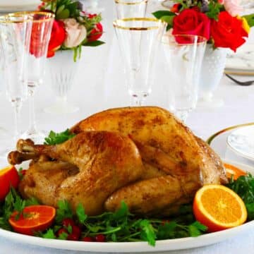 Square image of a whole roasted turkey on a platter with parsley and oranges around it.