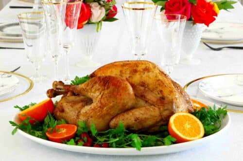 Horizontal image of a whole roasted turkey on a platter with parsley and oranges around it.