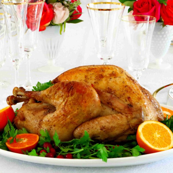 Horizontal image of a whole roasted turkey on a platter with parsley and oranges around it.