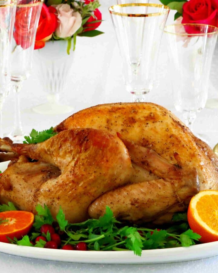 Horizontal image of a whole roasted turkey on a platter with parsley and oranges around it.