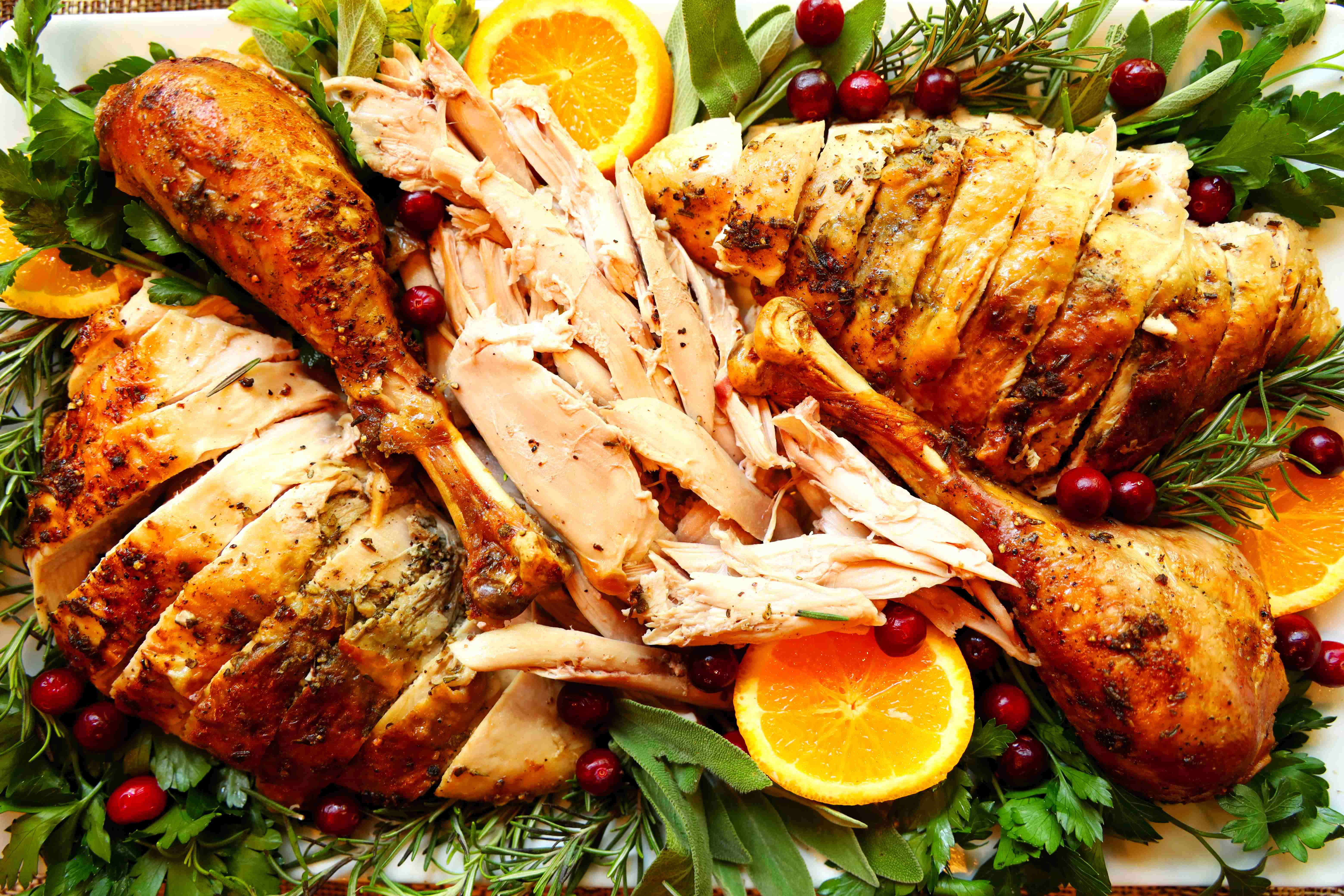 Turkey cut up on a platter with parsley and oranges and cranberries around it.