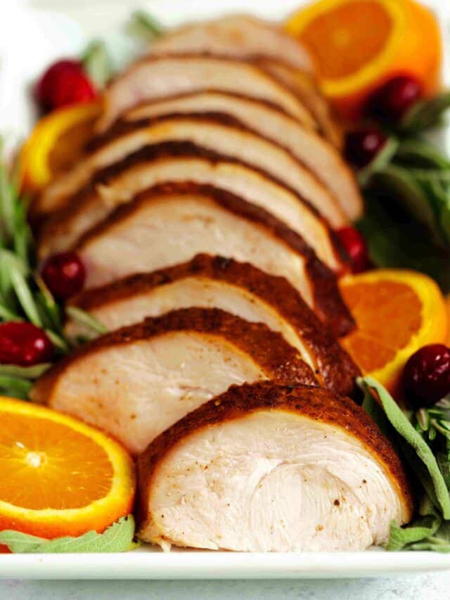 Sliced Smoked Turkey Breast on a platter with rosemary, cranberries, and orange slices