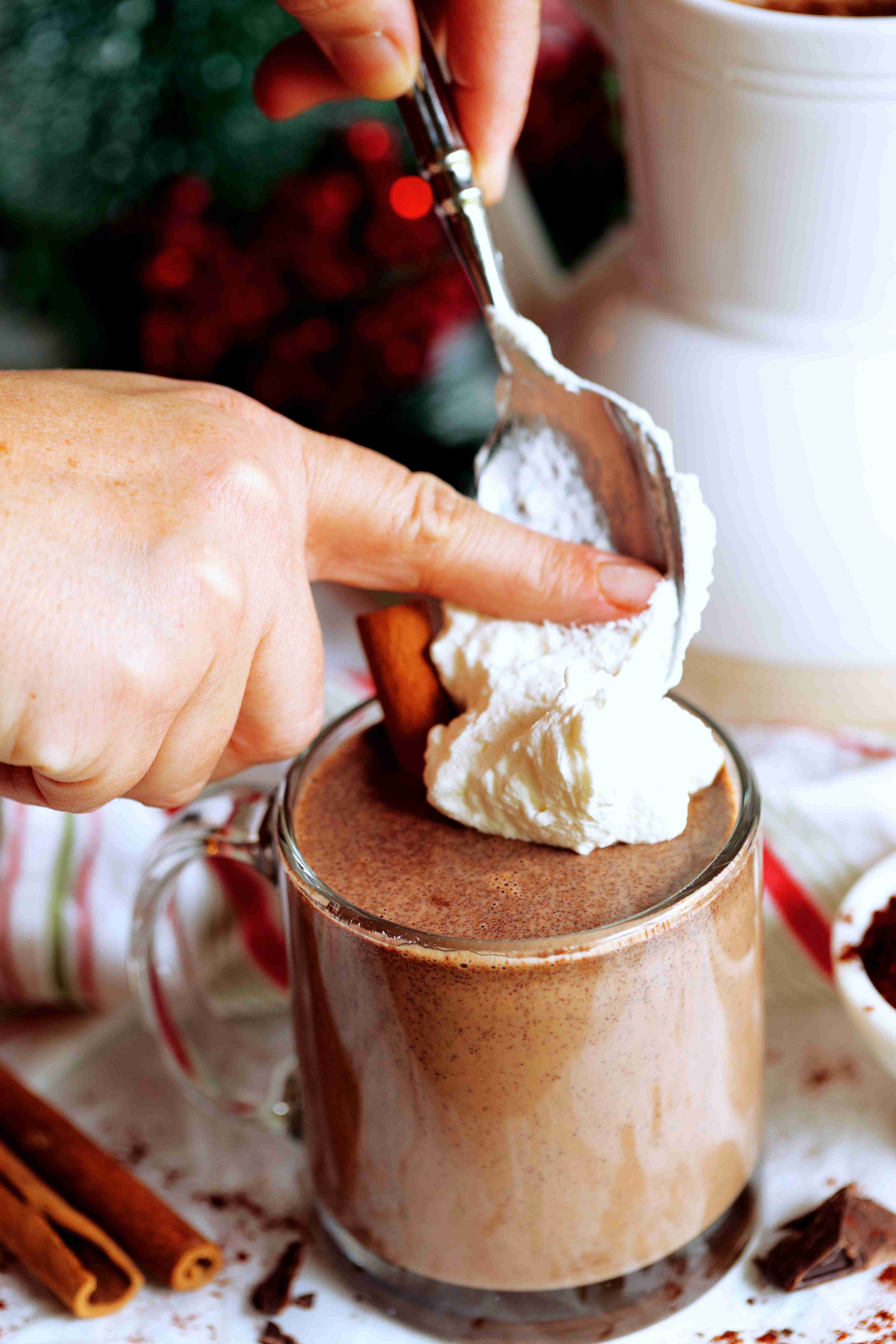 Whipped cream being added to the top of Mexican Hot Chocolate with a cinnamon stick