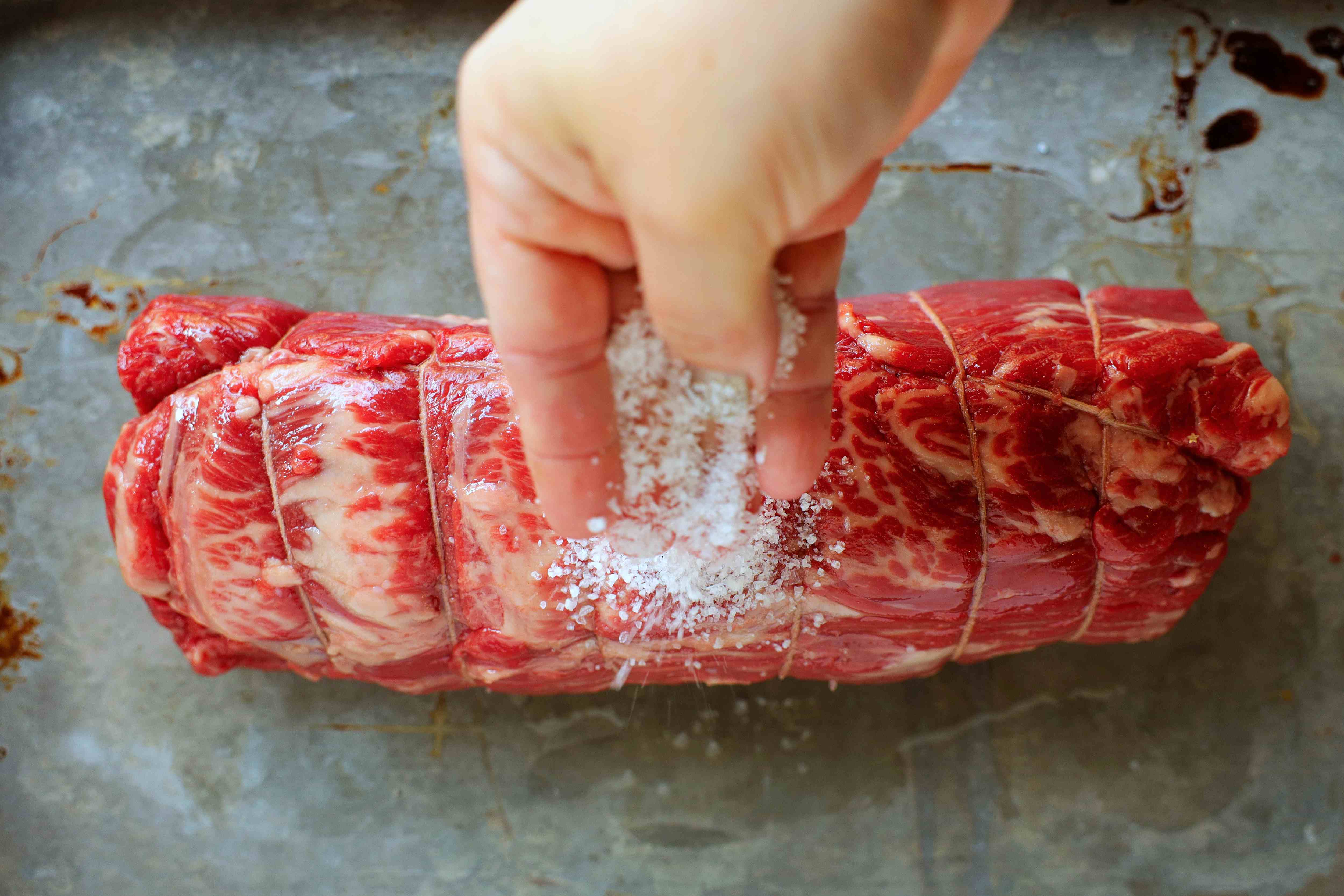 String-tied, marbled beef tenderloin being sprinkled with salt before going into the oven