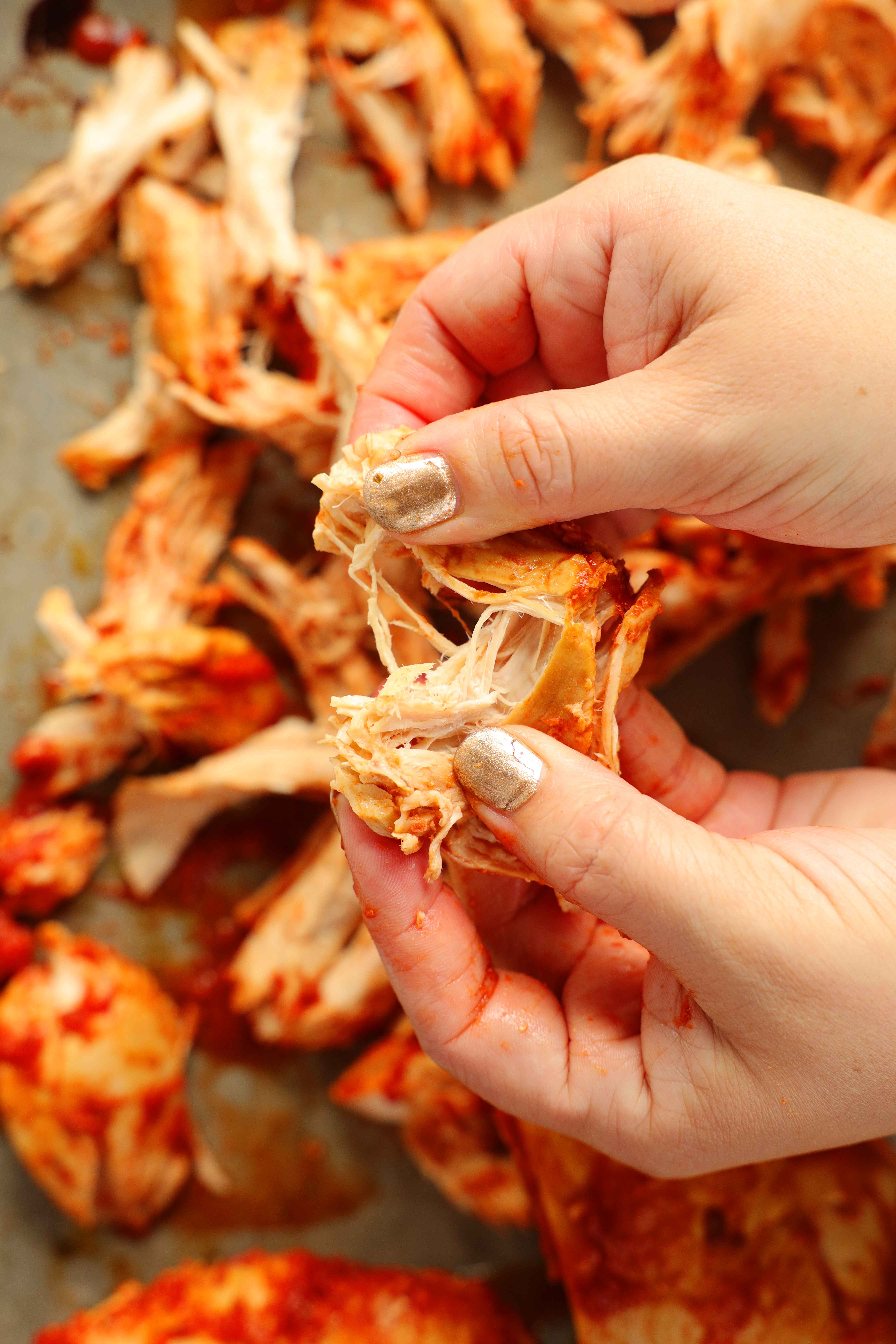Close-up of cooked chicken breast in Tinga de Pollo sauce being shredded by hand