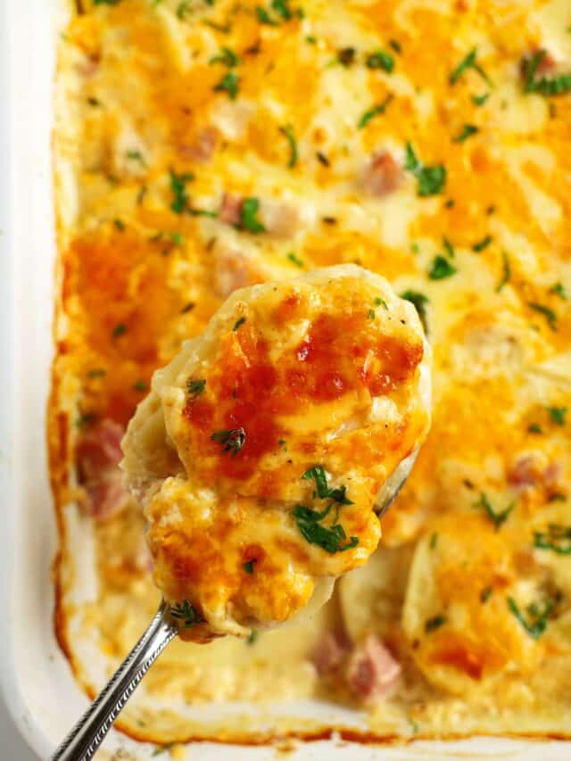 An overhead shot of a casserole dish with scalloped potatoes and ham with a spoon resting in the dish.