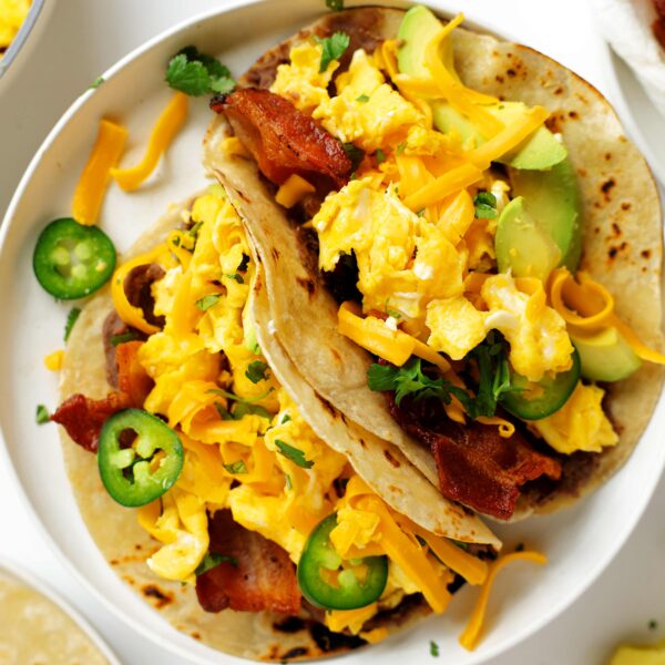 Overhead shot of bacon and egg Breakfast Tacos with avocado, cilantro, jalapenos, and grated cheddar cheese on flour tortillas.