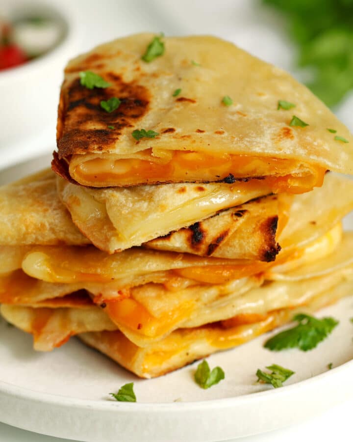 Cheese Quesadillas cut into quarters and stacked on a white plate with fresh cilantro