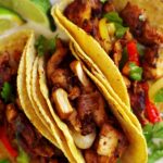 3 chicken fajita tacos on a white plate with lime wedges and cilantro off to the side.