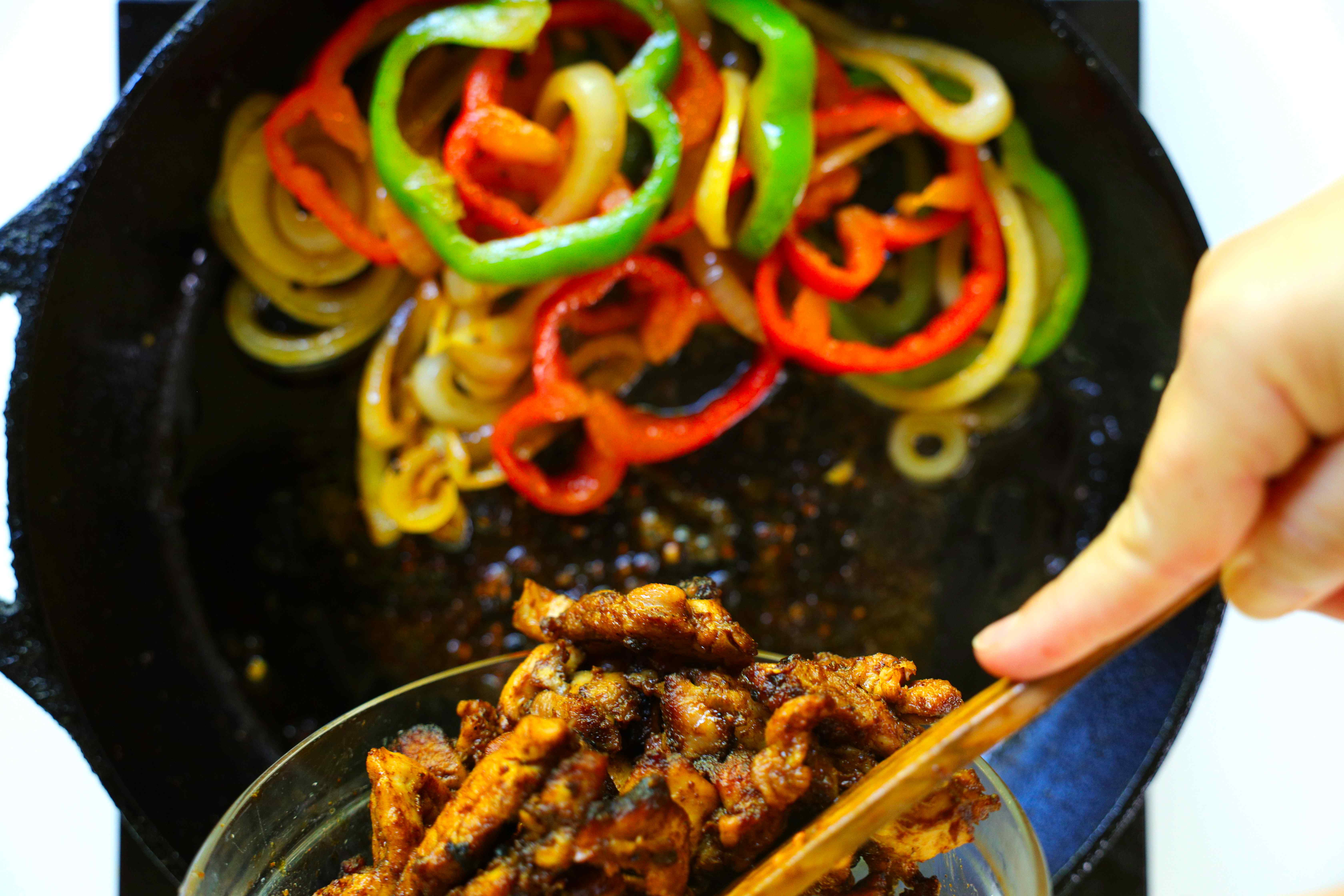 Cooked chicken thighs for Chicken Fajitas being added back to the cast iron skillet with sauteed peppers and onions.