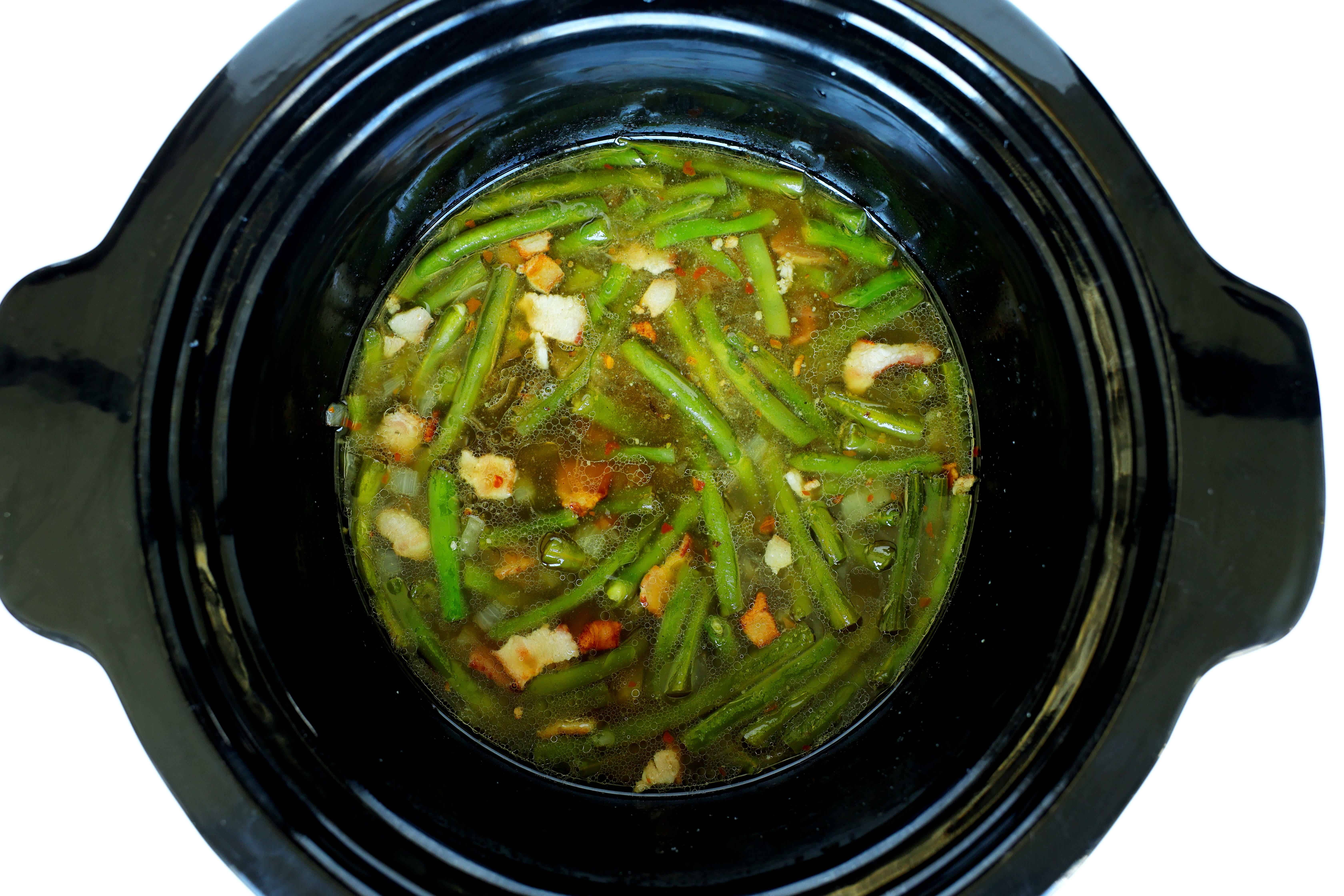 Green beans cooking in a crockpot with bacon, onion, chicken broth