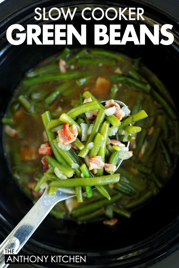 Pin for Pinterest | A spoon full of green beans with bacon and onion on top. The spoon is being held over a black crockpot.