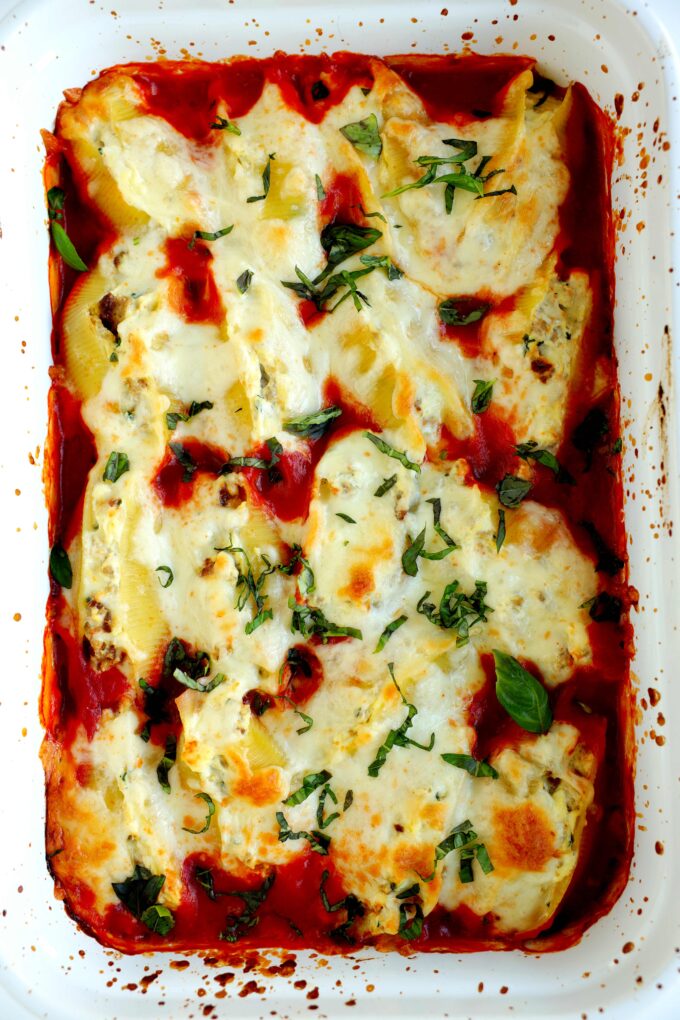 Baked stuffed shells with meat topped with ricotta, mozzarella, and Parmesan cheese in a white casserole dish