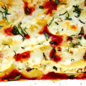 Close up of baked stuffed shells with meat topped with ricotta, mozzarella, and Parmesan cheese in a white casserole dish