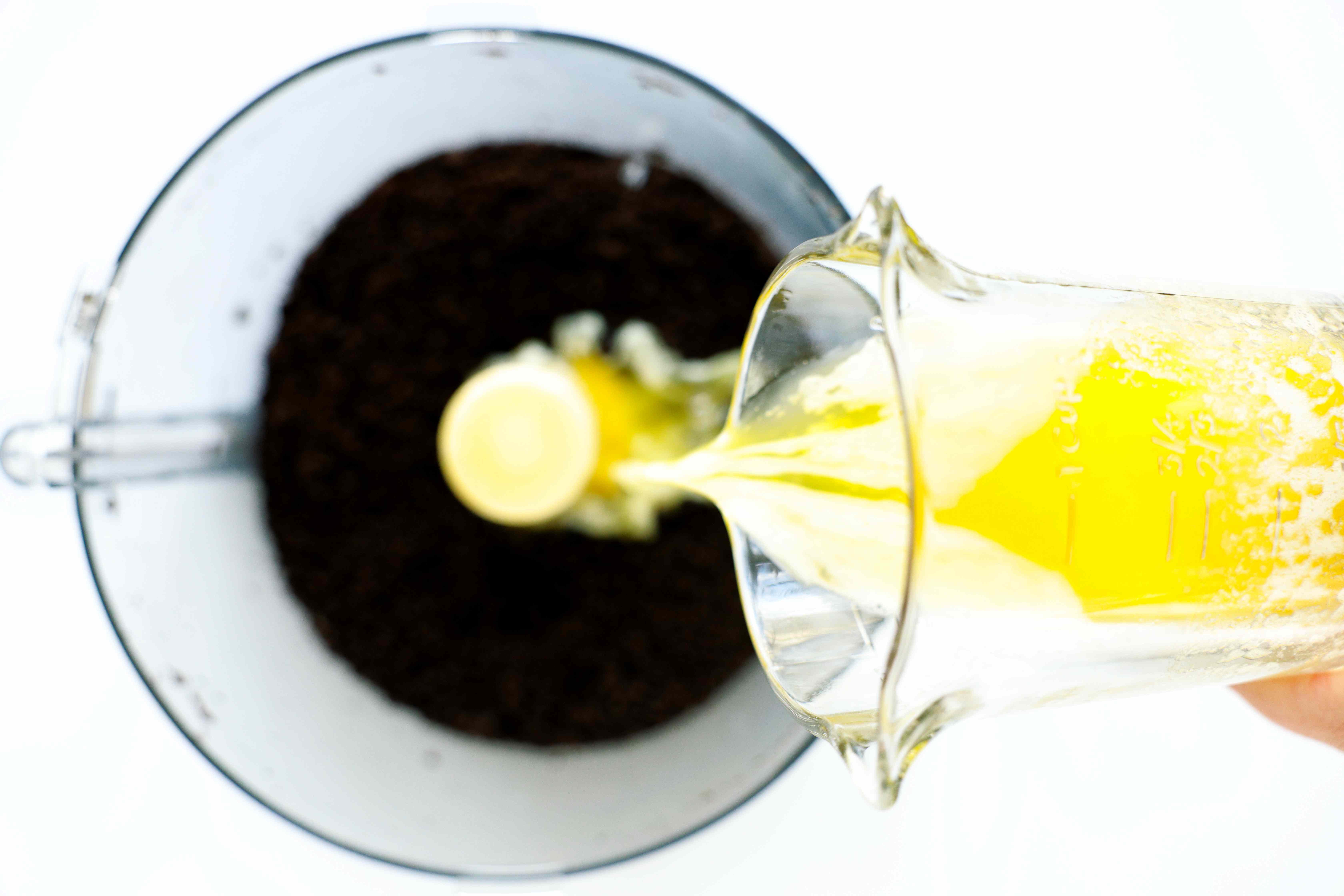 Melted butter being poured into a food processor with crushed Oreos