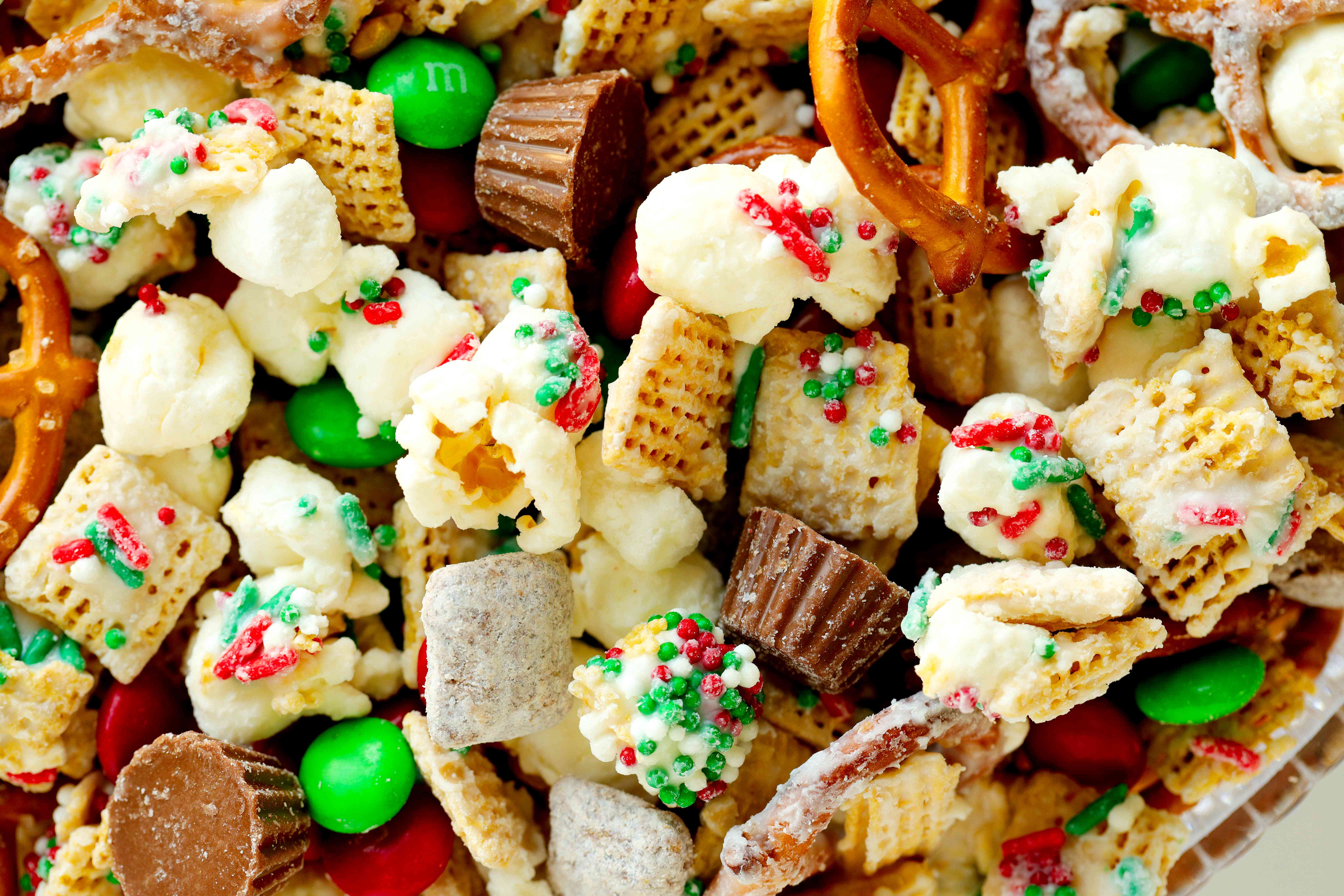 Christmas snack mix featuring popcorn, Reese's, pretzels, cereal, puppy, chow, and white chocolate. There are sprinkles on top.