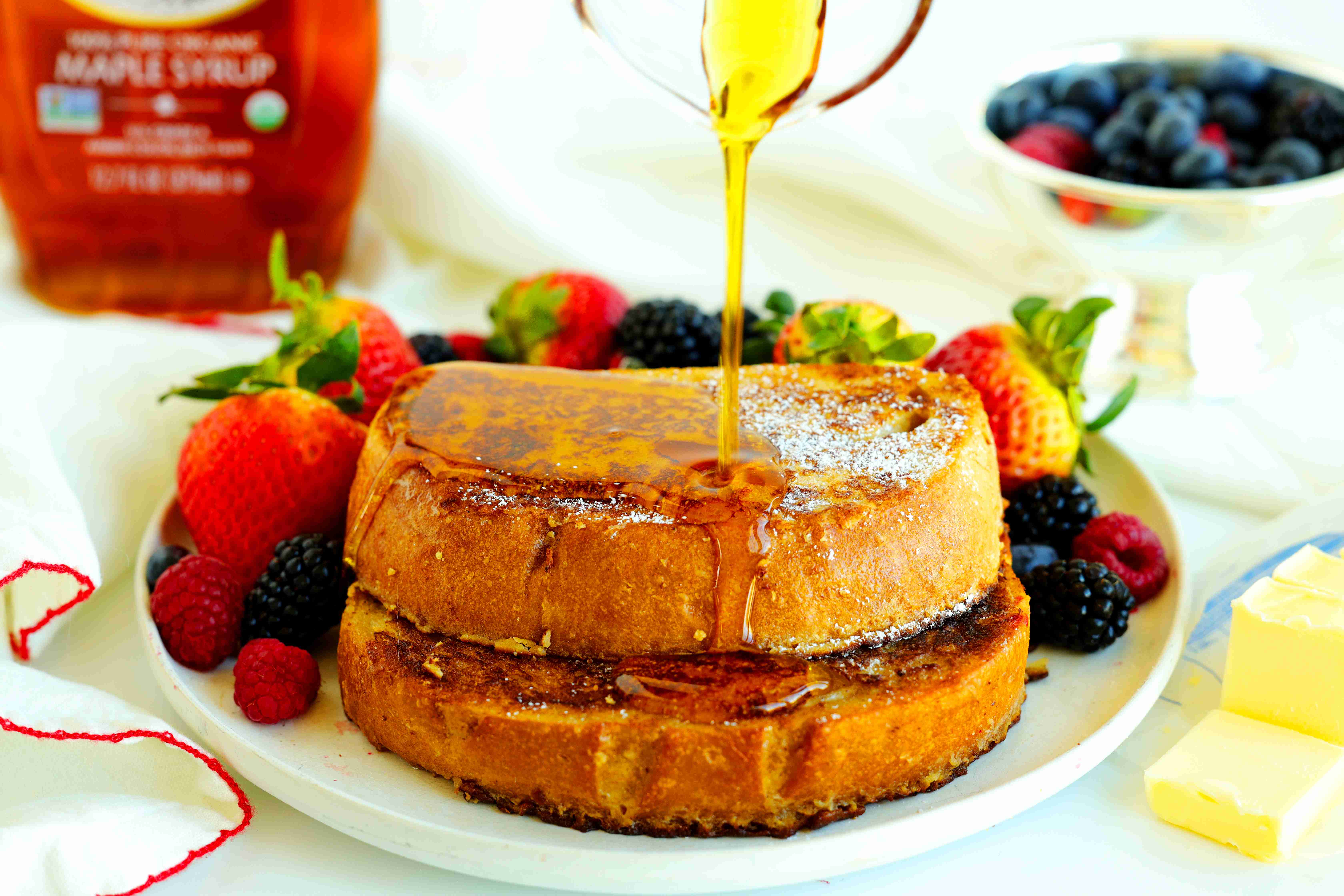 Sourdough French toast with fresh berries and maple syrup being poured over top
