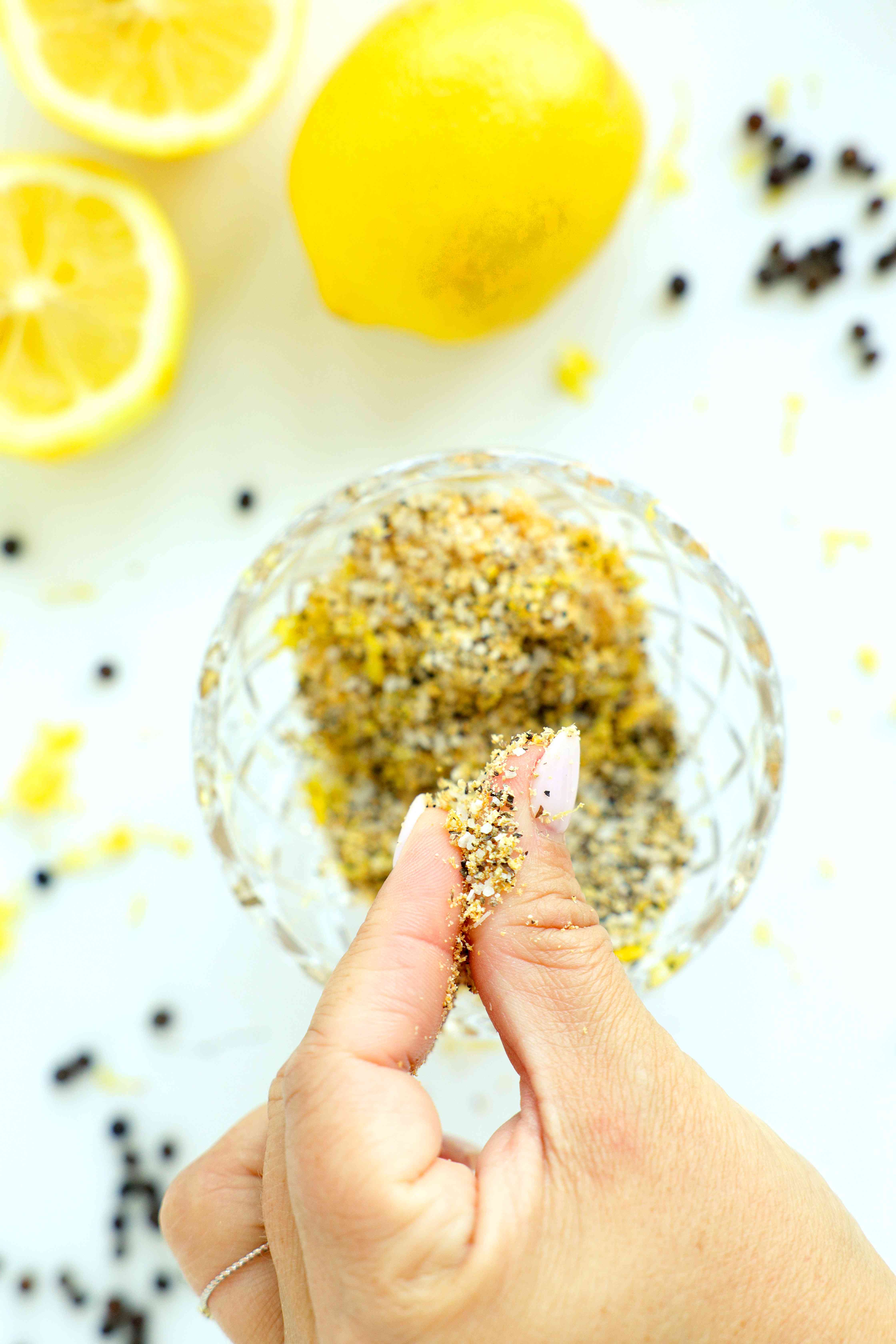 Rubbing Lemon Pepper Seasoning between fingers to combine over a glass bowl