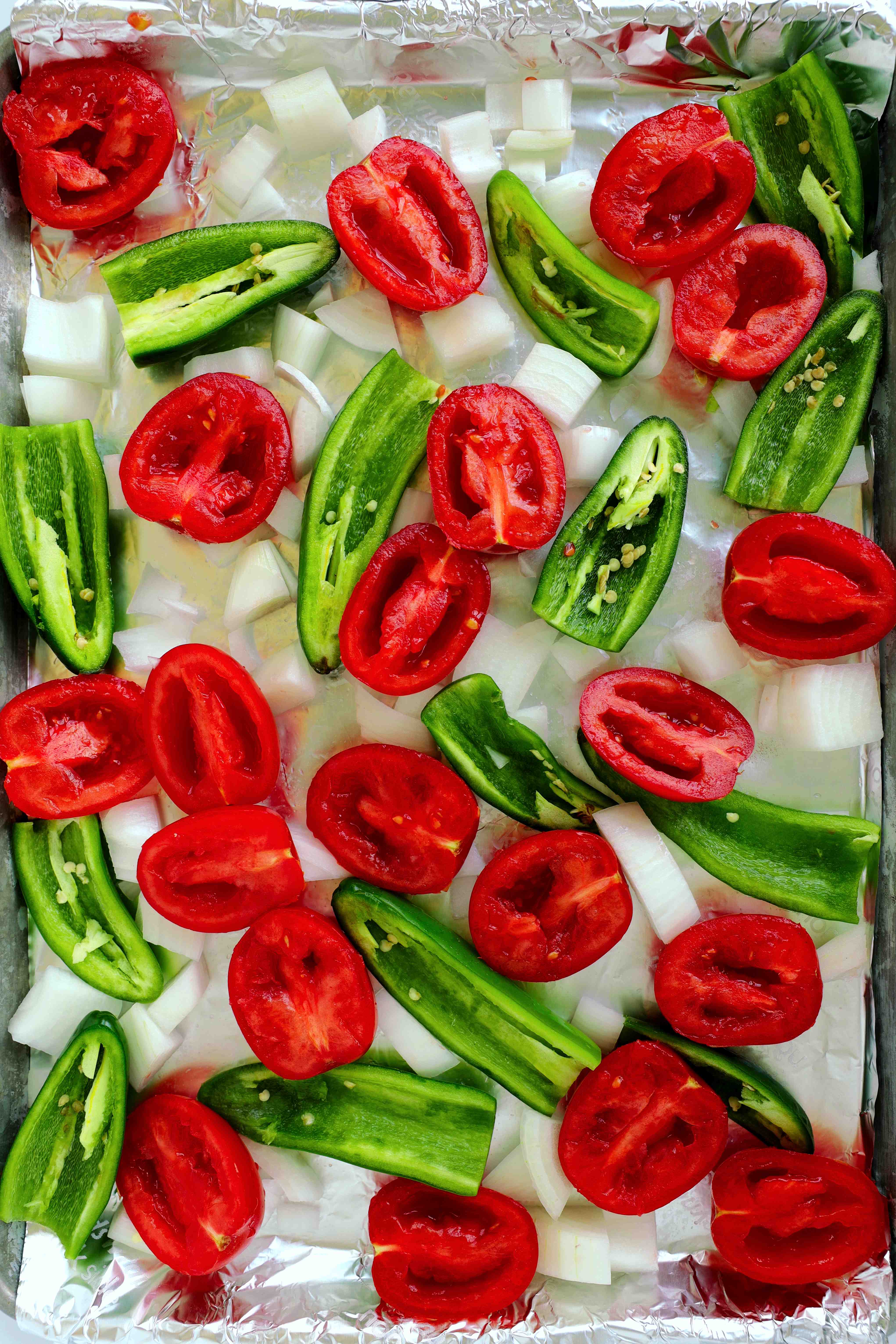 Not-yet-roasted tomatoes, jalapenos, and onions on a baking sheet for salsa ranchera